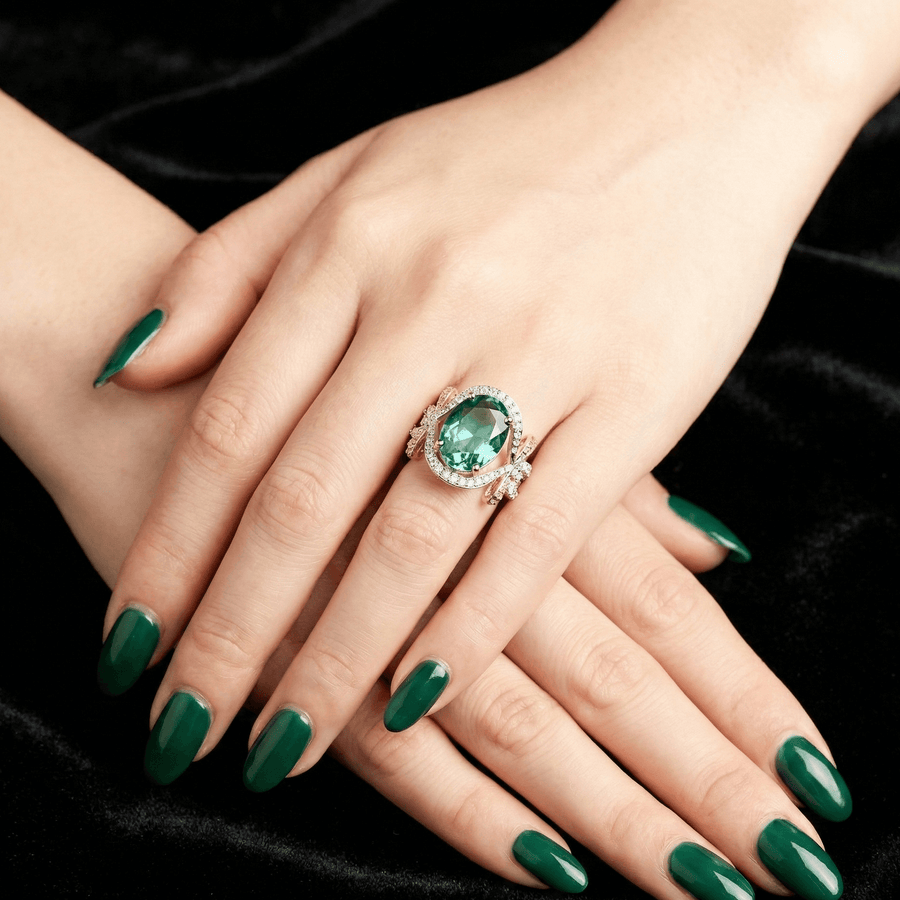 Green gemstone bow ring worn on a woman's hand with green manicure against a black velvet background