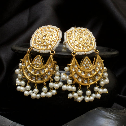 Close-up of gold-toned Kundan Jhumka earrings with kundan stones and white pearl tassels displayed on a black pot with black satin background