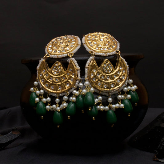 Gold-toned Kundan Jhumka earrings with kundan stone embellishments, white pearls, and green bead tassels against a dark background