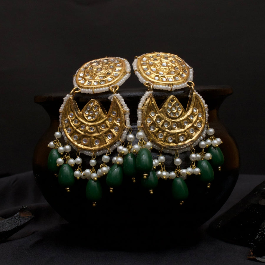 Gold-toned Kundan Jhumka earrings with kundan stone embellishments, white pearls, and green bead tassels against a dark background