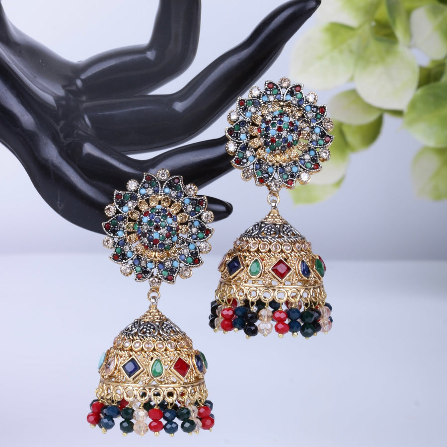 Pair of multicolor floral jhumka earrings with gold plating and dangling red, black, and clear beads displayed on a black hand-shaped stand.
