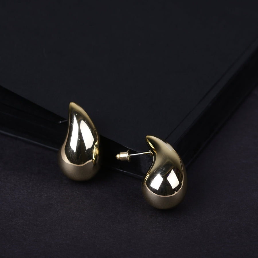 Gold-toned polished teardrop stud earrings with smooth reflective surface on black background