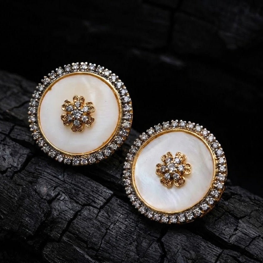 Round stud earrings with white mother of pearl centers and sparkling stone halos placed on dark textured surface