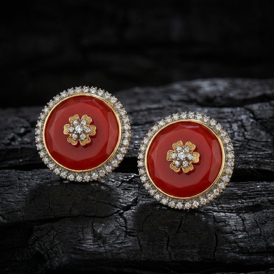 Red round stud earrings with flower motif and sparkling stone halos set on dark textured surface