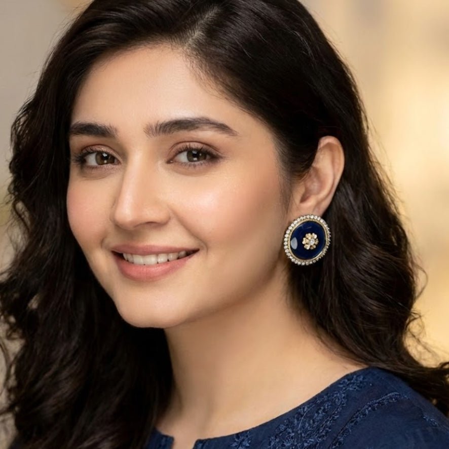 Model showcasing navy blue round stud earrings with sparkling stone halos while smiling, dressed in a matching navy embroidered outfit