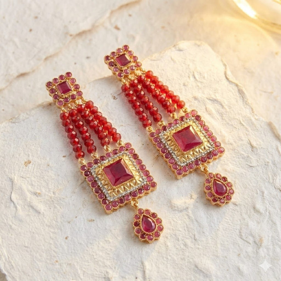 Red gemstone bead earrings displayed on textured white stone background