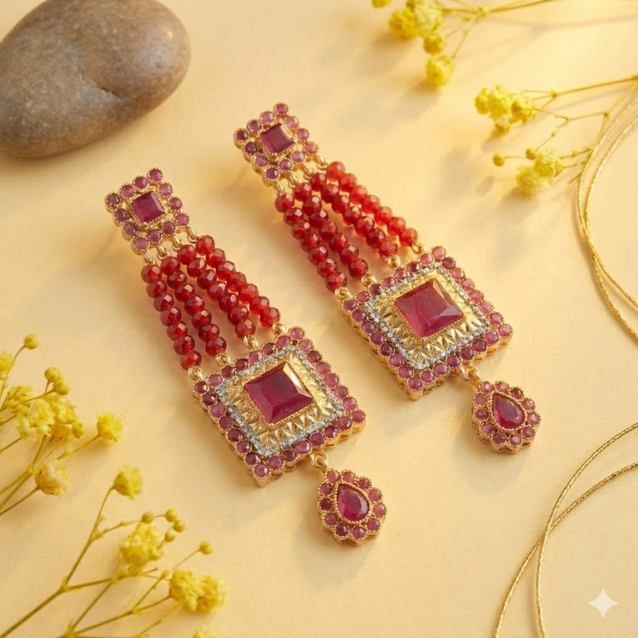 Red gemstone bead earrings styled on warm yellow surface with flowers