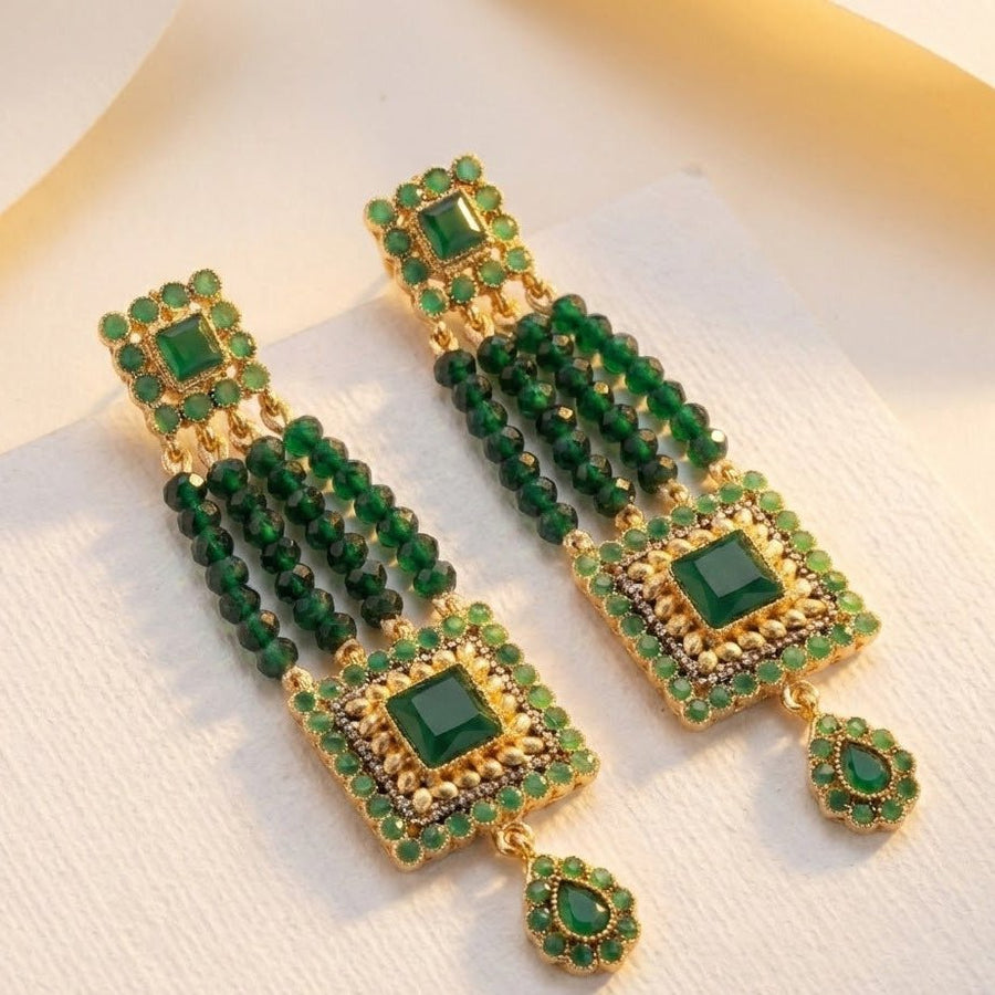Close-up of hand holding green gemstone earrings against natural outdoor background