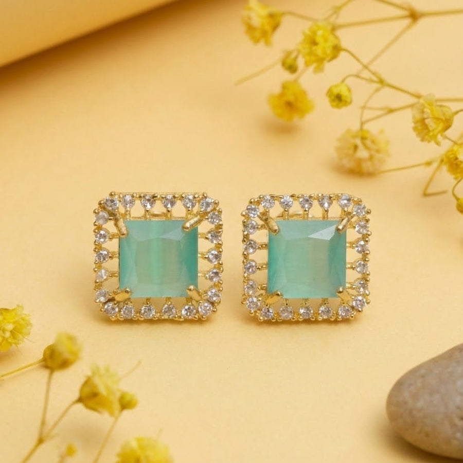 Mint green halo stud earrings with gold-tone setting displayed on light surface with small yellow flowers