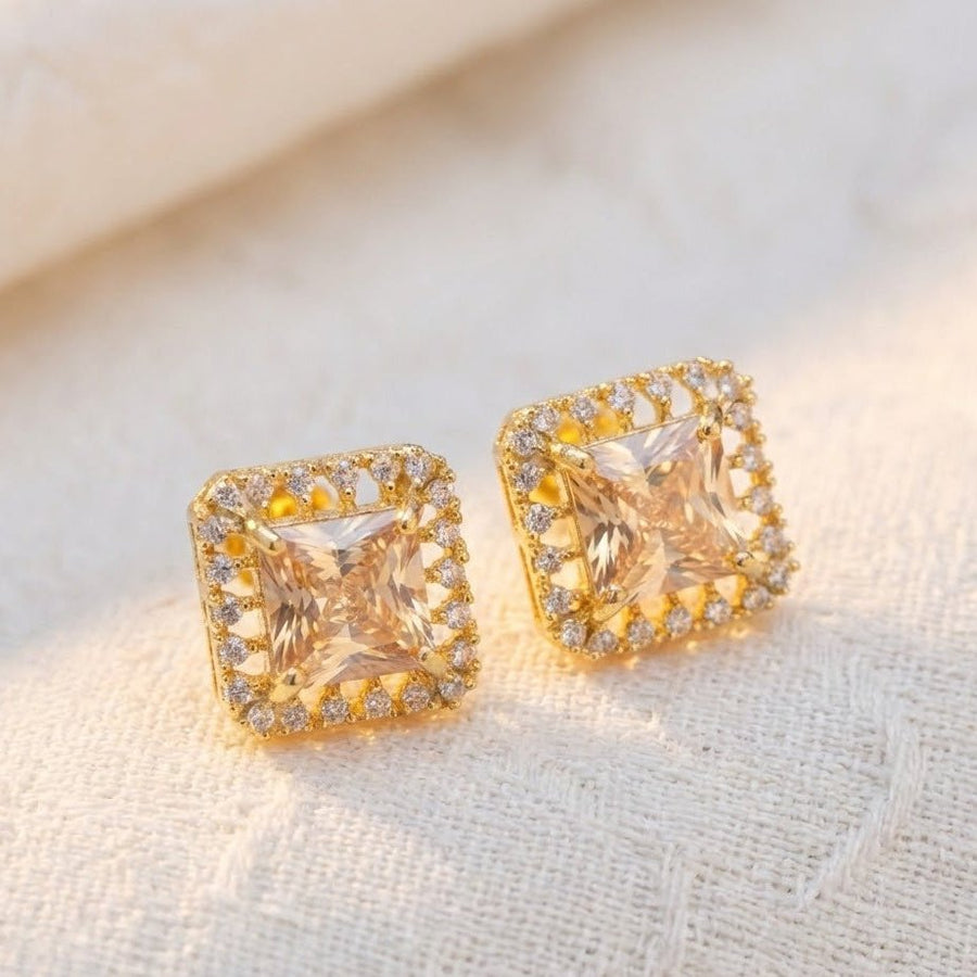 Champagne square halo stud earrings on cream-colored fabric surface showing design details and sparkle