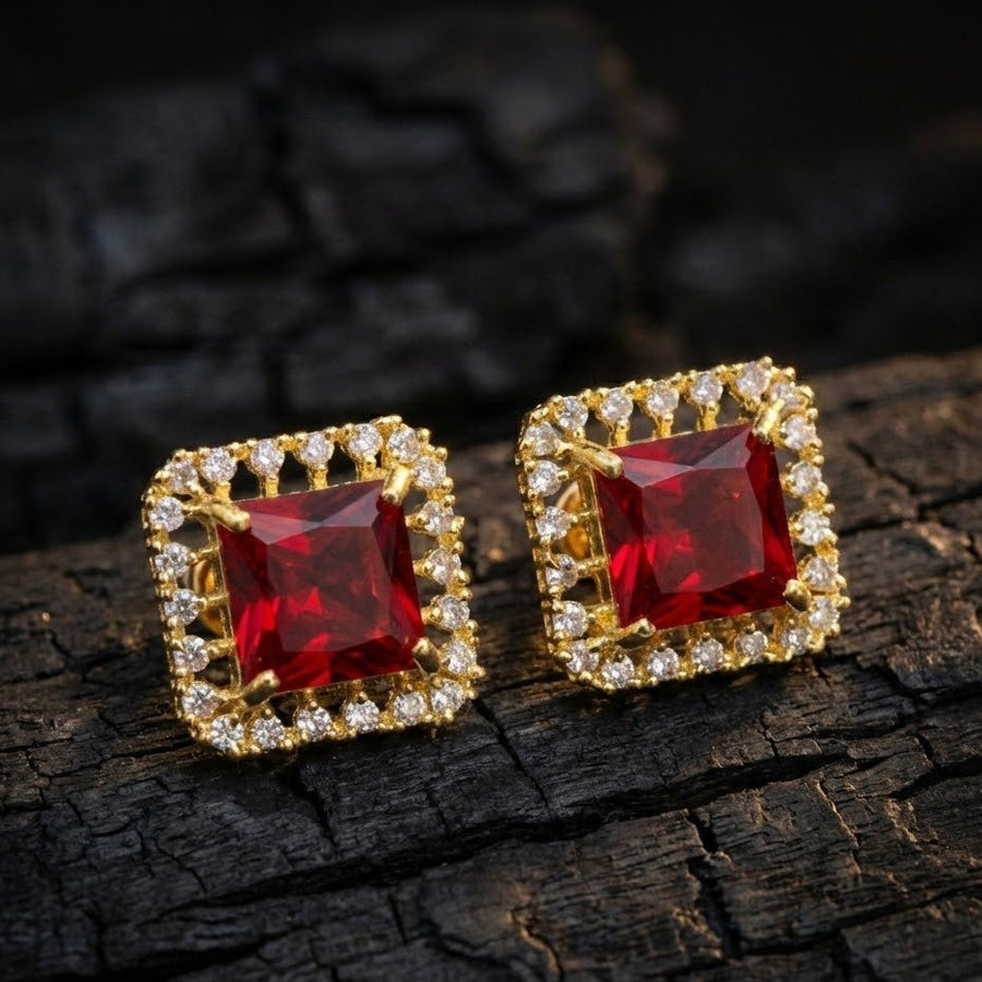 Close-up view of red halo stud earrings placed on textured dark surface showcasing gold-tone metal and sparkling round stones