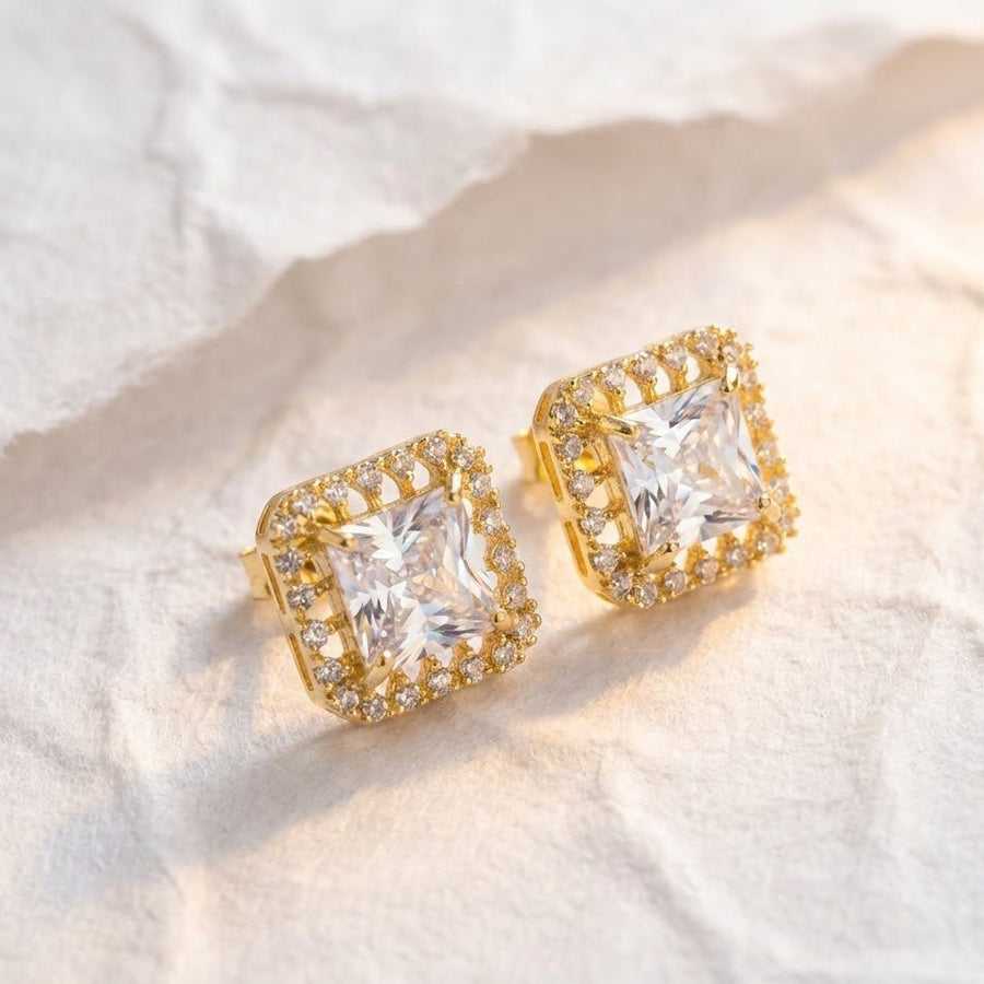 Clear square halo stud earrings displayed on soft cream surface under natural light highlighting sparkle