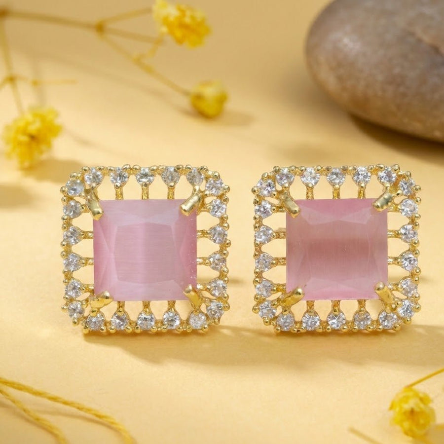 Pink square halo stud earrings placed on textured dark surface focusing on color contrast and shine