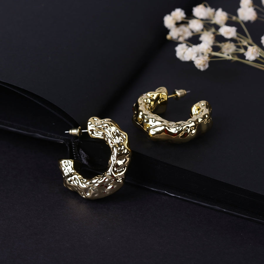 Pair of polished gold textured hoop earrings on dark background with white dried flowers