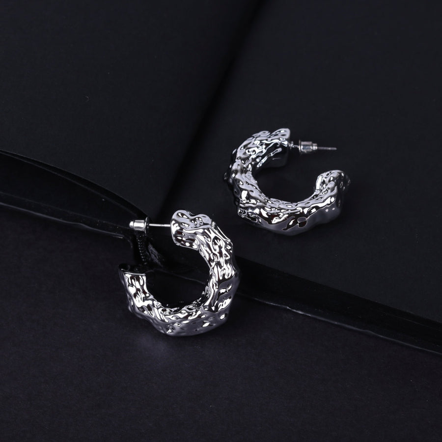 Pair of shiny textured silver hoop earrings on dark background