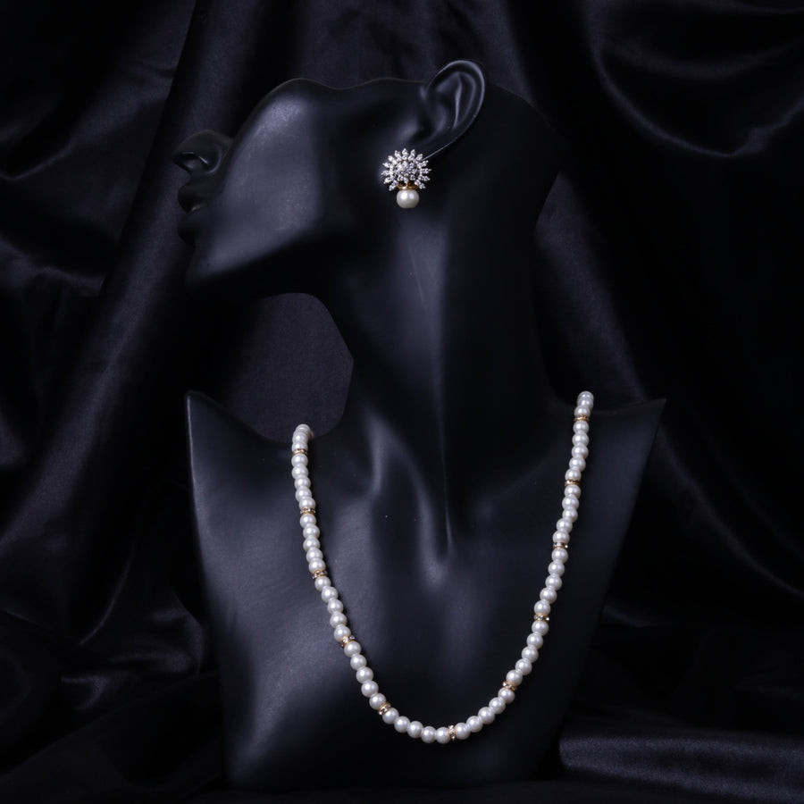 Black mannequin wearing matching pearl necklace and crystal floral earrings against black silk background