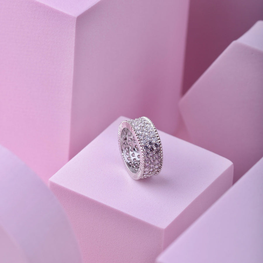 Silver-tone version of the wide band cubic zirconia ring resting on a pink geometric display