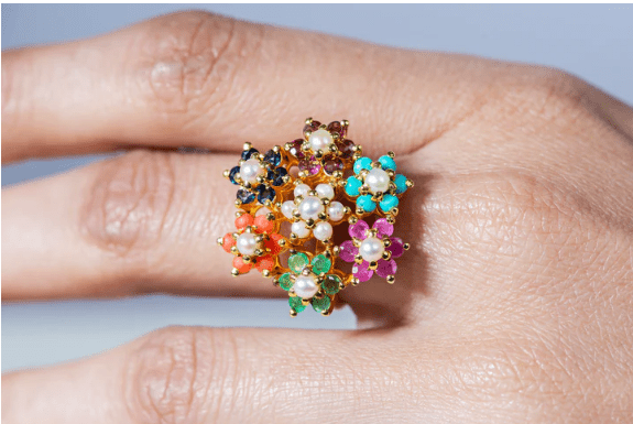 Close-up of a woman’s hand wearing the multicolor floral zircon ring with visible intricate flower details and vibrant colored zircon stones on a light background