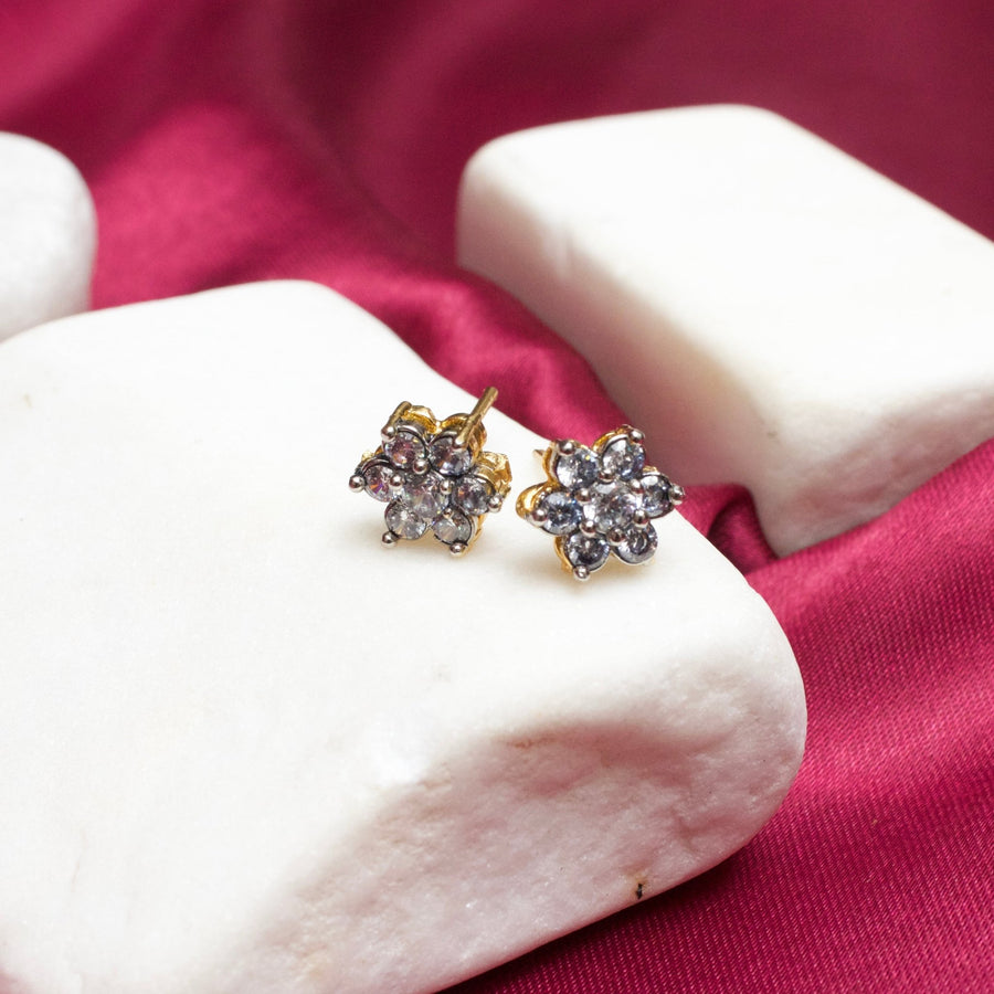 Pink gemstone floral stud earrings with gold plating on white stone display and magenta fabric background
