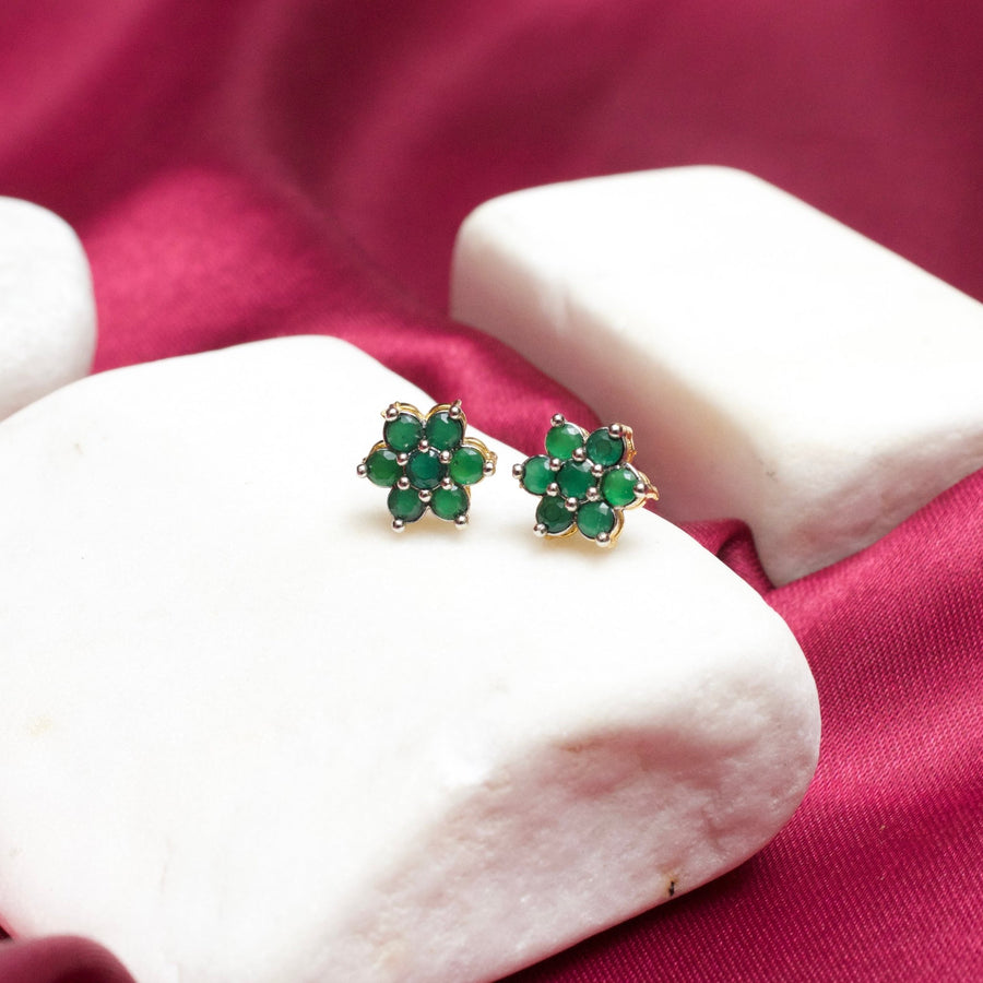 Green floral gemstone stud earrings with gold-plated setting on white stone display with magenta fabric background