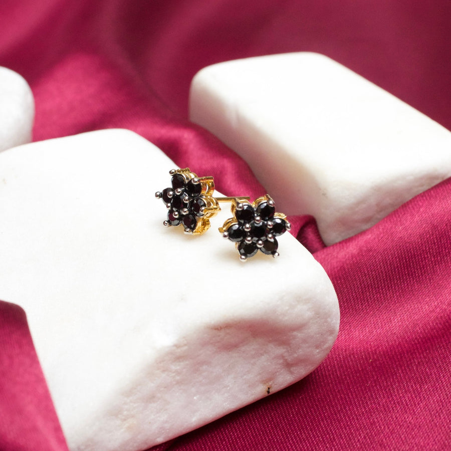 Black gemstone floral stud earrings with gold plating on white stone display with magenta fabric background