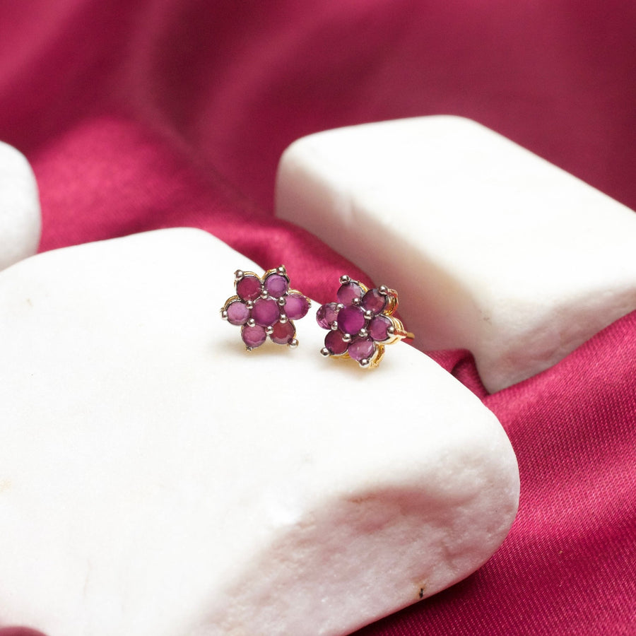 Clear gemstone floral stud earrings with gold plating positioned on white stone display with magenta fabric background