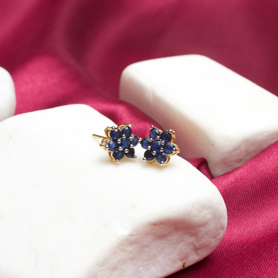Blue floral gemstone stud earrings with gold plating on white stone display and magenta fabric background